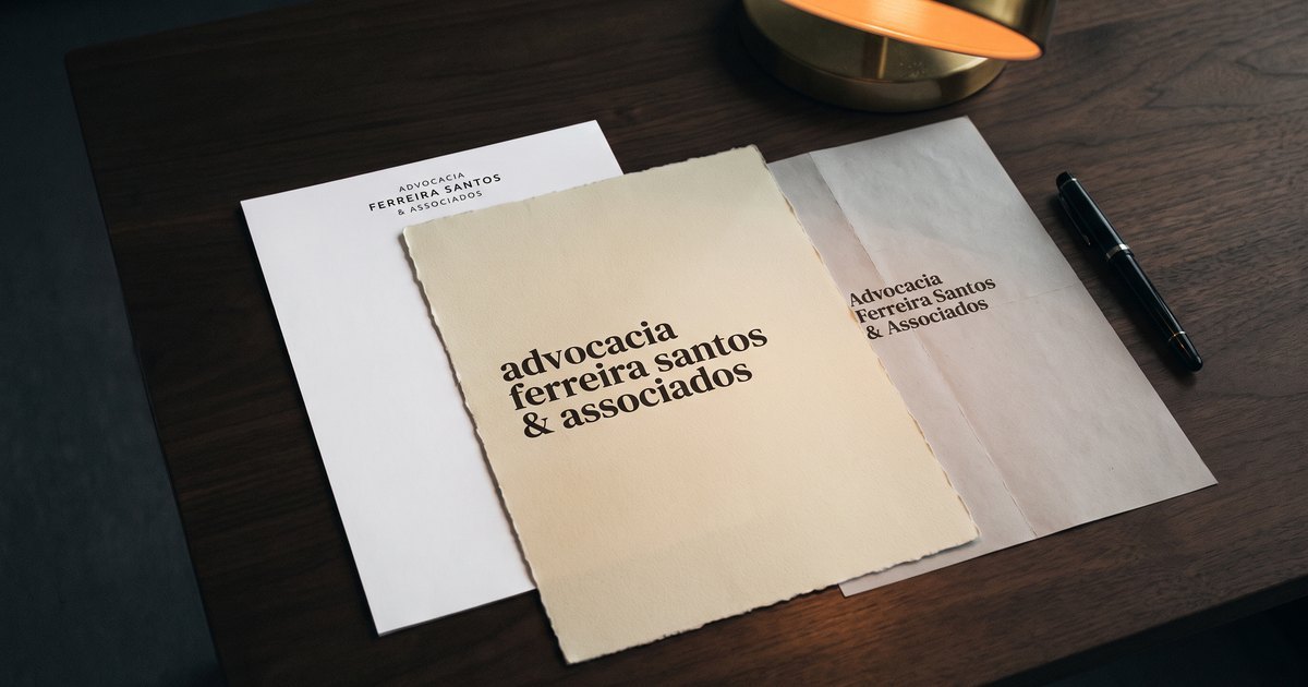Três folhas de papel timbrado do mesmo escritório de advocacia sobre uma mesa de madeira escura, cada uma com o nome impresso numa tipografia, num tamanho e numa posição diferentes